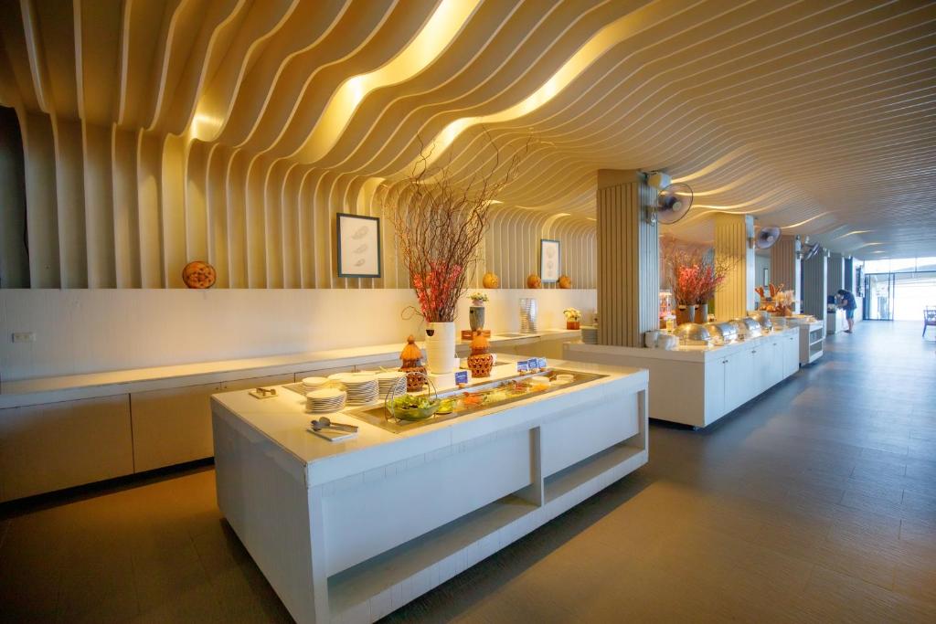 Mūsdienīgs restorāna interjers ar viļņotām sienām un elegantu bufeti, kurā ir dažādi ēdieni un dekoratīvi elementi. Telpa ir gaiša un plaša, radot patīkamu atmosfēru.