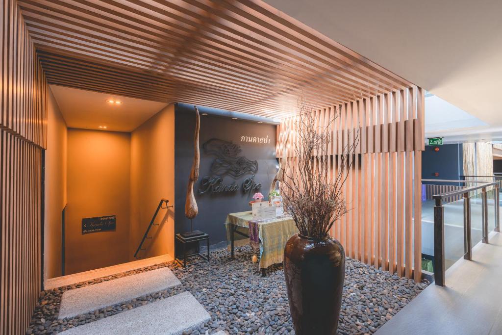 Elegants spa ieejas dizains ar koka apdari un akmeņiem, radot mierīgu atmosfēru. Uz galda redzama ziedu kompozīcija un informācija par pakalpojumiem.