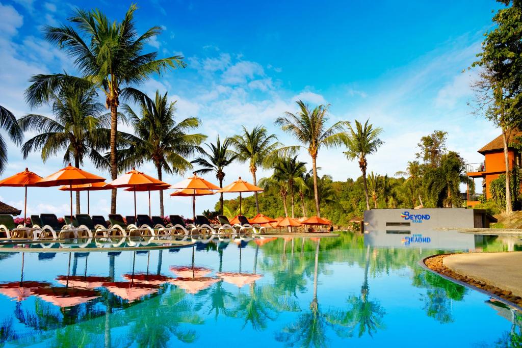 Luksusa viesnīcas baseins ar palmām un saulessargiem, kas atspoguļojas ūdenī. Ideāla atpūtas vieta tropiskā vidē.