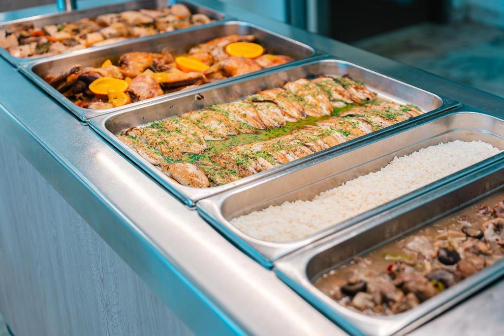 Dažādu ēdienu bufete ar ceptu gaļu, zivīm un rīsiem, kas pasniegta metāla traukos.