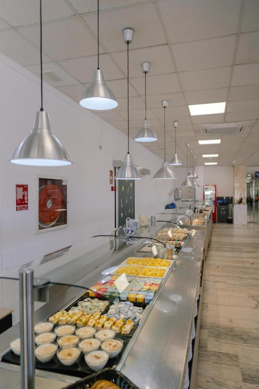 Moderns bufetes galds ar plašu pārtikas izvēli, apgaismots ar stilīgām metāla lampām. Svaigi izskatīgi ēdieni un deserts ir izvietoti gar garo galdu.