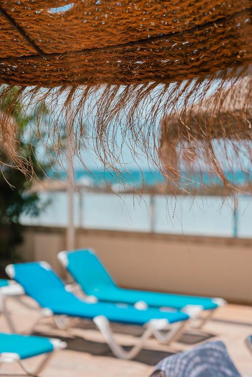 Saulainā pludmales atpūtas zona ar zilo sauļošanās krēslu rindu un saules aizsargu. Rāmā atmosfēra pie jūras, ideāla relaksācijai.