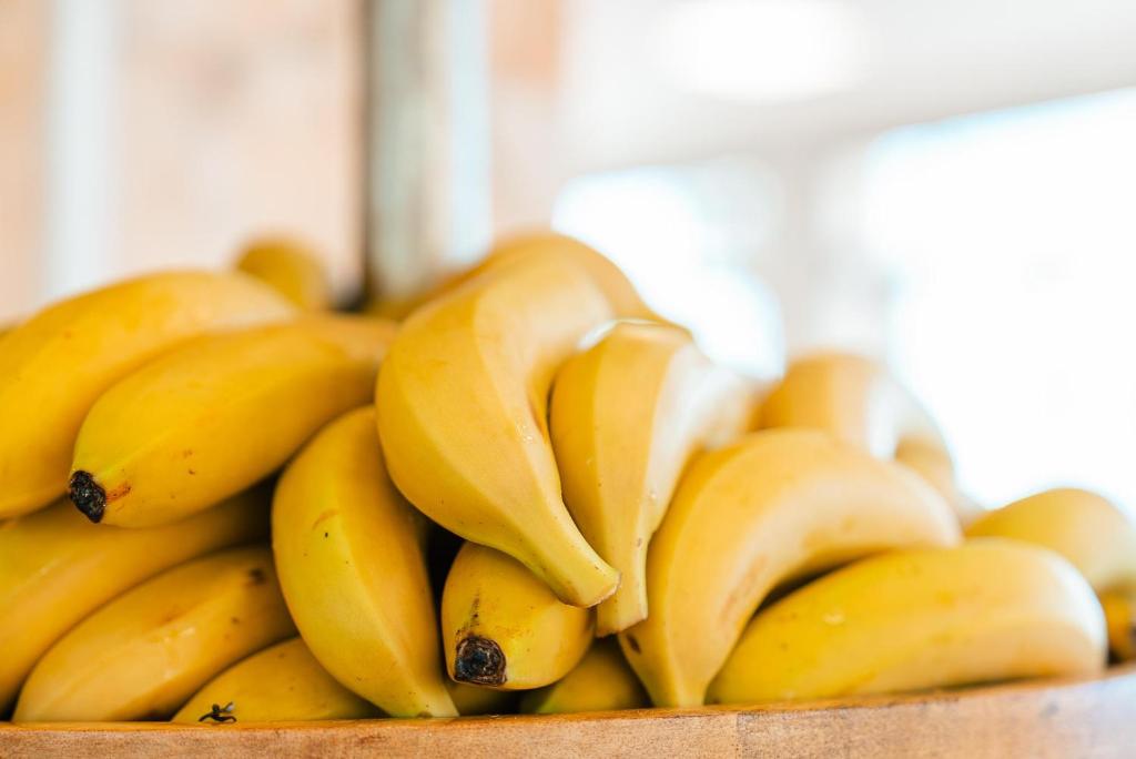 Dzelteni banāni sakrautā kaudzē, atrodas koka traukā ar izplūdušu fona.