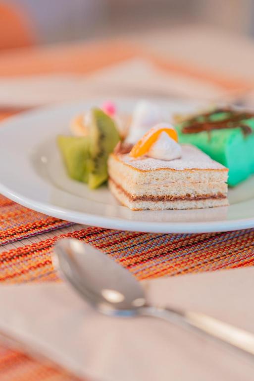 Deserts uz šķīvja, ieskaitot krēmīgu kūku ar mandarīnu un zaļo saldējumu, pasniegti uz krāsainas galdautas.