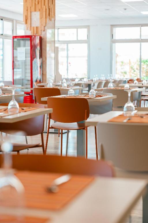 Moderns restorāns ar elegantiem galdiem un krēsliem, kas dekorēti ar glāzēm un galda piederumiem. Gaismas apstākļi rada patīkamu atmosfēru.