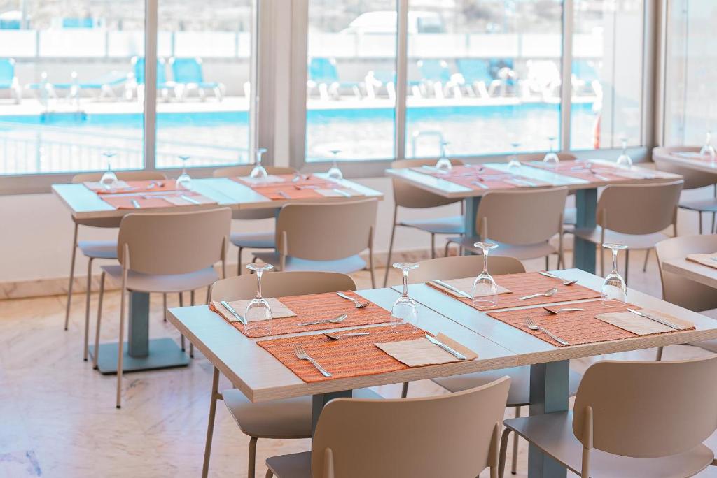 Mūsdienīgs restorāna interjers ar skatu uz baseinu, kur galdos ir oranži galdauti un galda piederumi.