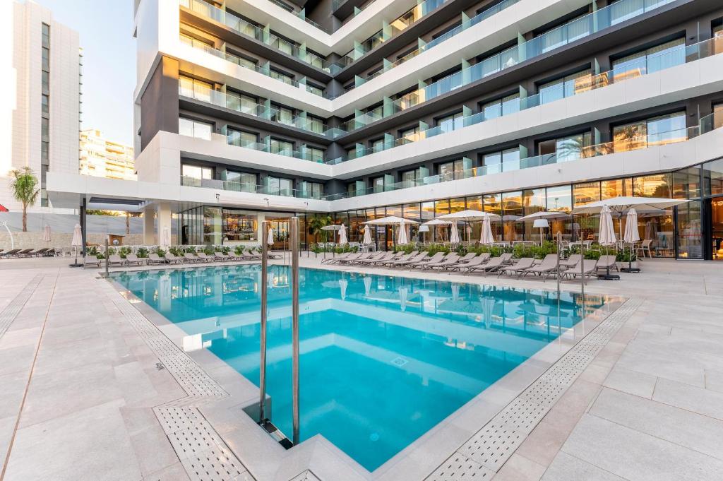 Mūsdienīgs viesnīcas komplekss ar skaistu peldbaseinu un saulessargiem, ideāls atpūtai un relaksācijai. Komfortabli sauļošanās krēsli un zaļumi papildina patīkamo atmosfēru.