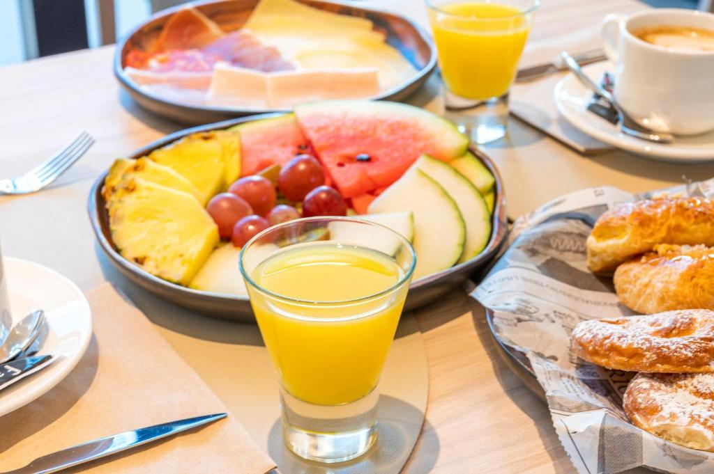 Krāsains augļu plate ar ananāsu, arbūzu, vīnogām un meloni, blakus glāze apelsīnu sulas un svaigi cepti kruasāni. Ideāls brokastu izvēle.