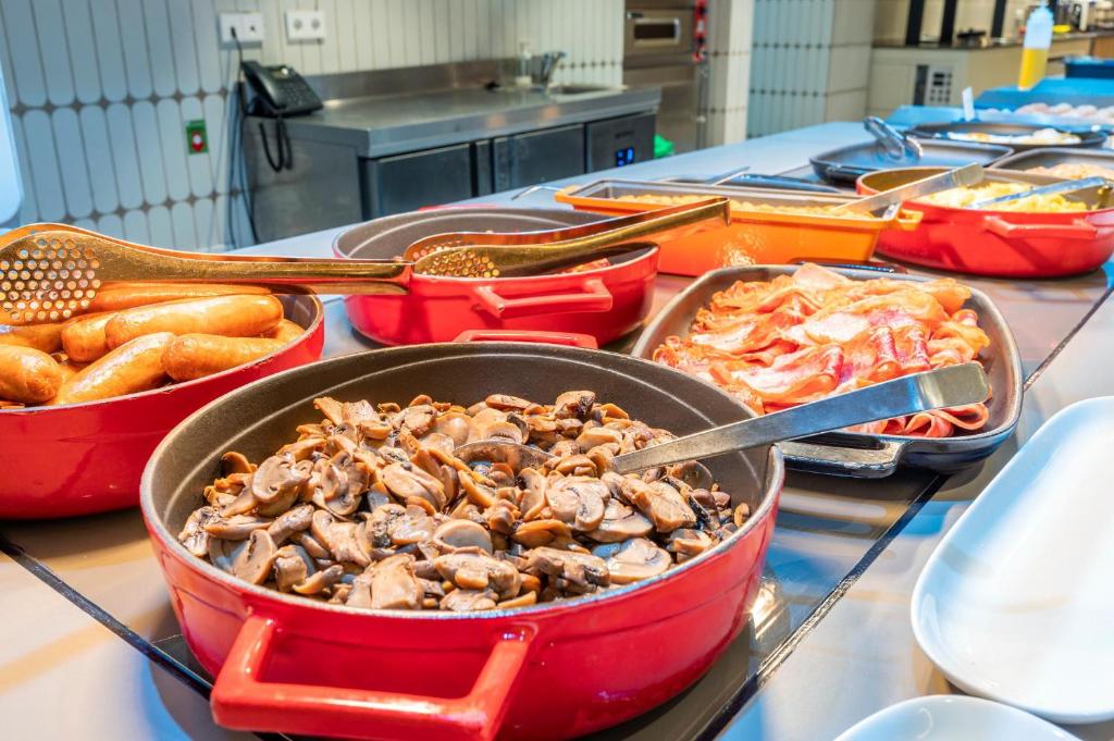 Svaigi pagatavoti ēdieni, tostarp desas un sēnes, pasniegti sarkanās pannās, izceļot brokastu bufeti.