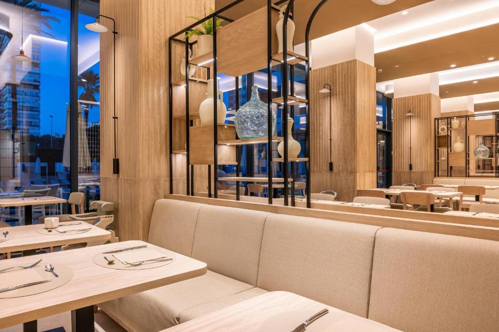 Mūsdienīgs restorāna interjers ar koka apdari, elegantiem galdiem un stilīgām dekorācijām. Telpa ir apgaismota ar siltu gaismu, radot patīkamu atmosfēru.