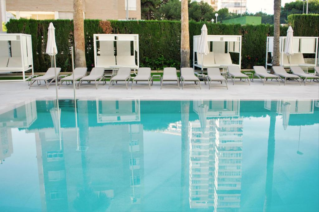 Baseins ar saulessargiem un sauļošanās krēsliem, atspoguļojot apkārtējo ainavu. Ideāla vieta atpūtai un relaksācijai.