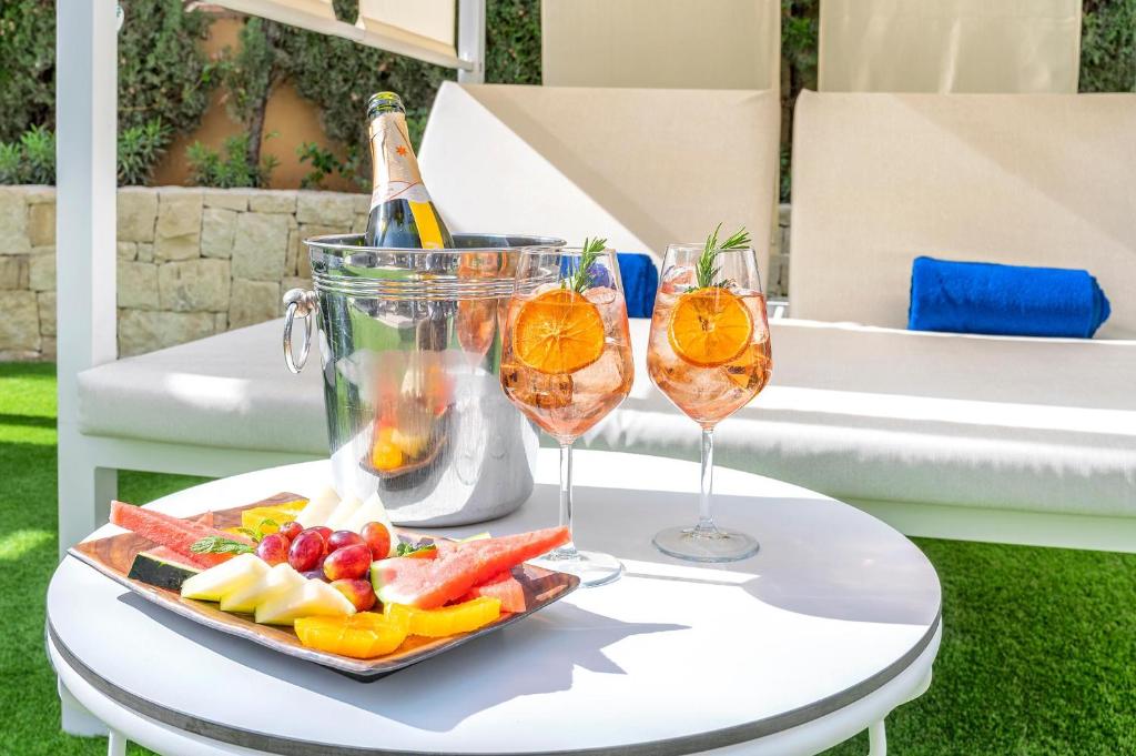 Šampanietis un augļu plate ar dzērieniem, kas pasniegti pie viesnīcas baseina uz baltas galdiņa, radot relaksējošu atmosfēru.