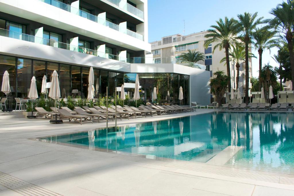 Mūsdienīgs baseins ar saulessargiem un sauļošanās krēsliem, apkārt palmām un modernām ēkām. Ideāla vieta atpūtai un relaksācijai.