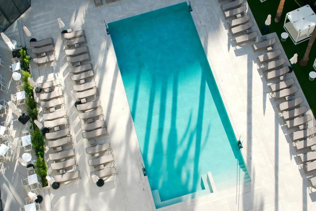 Mūsdienīgs peldbaseins ar saulessargiem un atpūtas krēsliem, kas izvietoti apkārt. Baseina ūdens ir dzidrs, un ap to ir zaļumi un terases mēbeles.