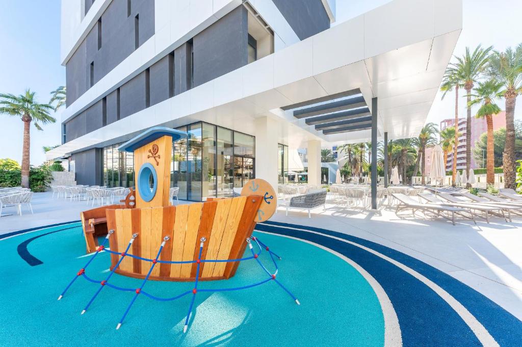 Bērnu spēļu laukumā ir koka kuģa forma, kas atrodas pie modernas viesnīcas ar palmām un atpūtas krēsliem. Šī vieta ir ideāla ģimenēm, kas meklē izklaidi un relaksāciju saulainā vidē.