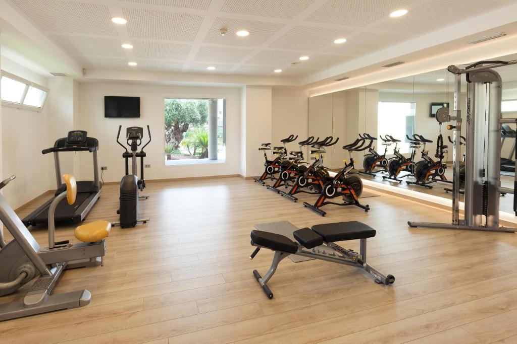 Mūsdienīgs sporta zāles interjers ar dažādām fitnesa iekārtām, tostarp skrejceliņu, velotrenažieriem un spēka trenažieriem, apgaismots ar dabiskiem gaismas avotiem.