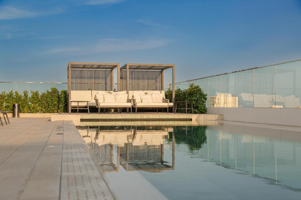 Mūsdienīgs jumta baseins ar elegantiem atpūtas krēsliem un koka nojumi, kas nodrošina komfortu un relaksāciju. Skats uz skaidru debesu un zaļumiem paplašina telpu un rada mierīgu atmosfēru.