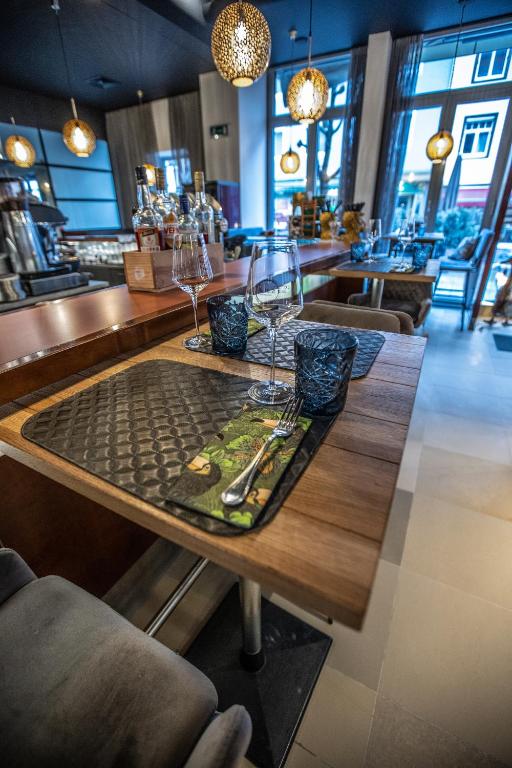 Elegants restorāna galds ar vīna glāzēm un dekoratīviem traukiem, apgaismotajiem griestu lampām un modernu interjeru. Ideāla vieta relaksējošai maltītei.