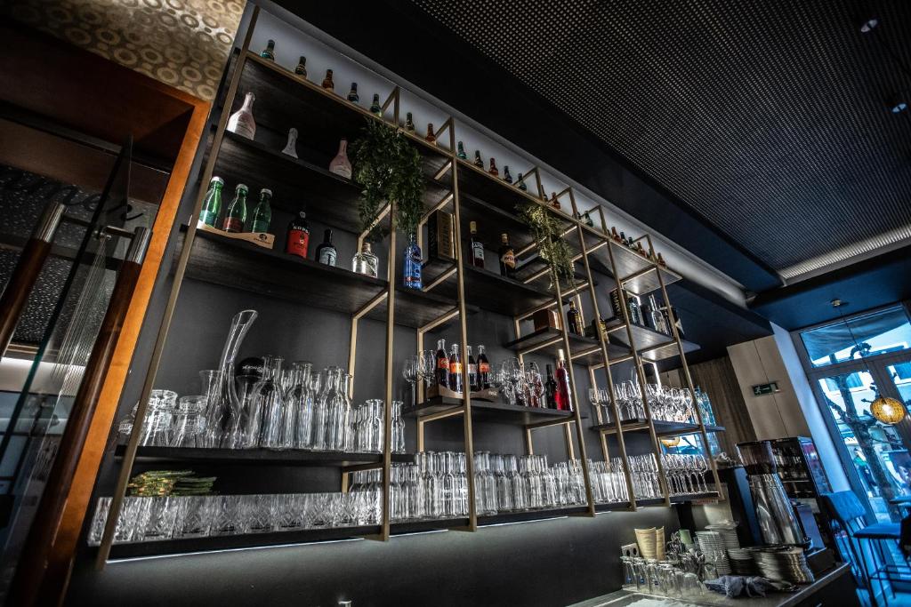 Elegants bāra plaukts ar dzērienu pudelēm un glāzēm, kas izkārtotas mūsdienīgā interjerā. Plauktā redzami dažādi dzērieni un dekoratīvi elementi, radot viesmīlīgu atmosfēru.