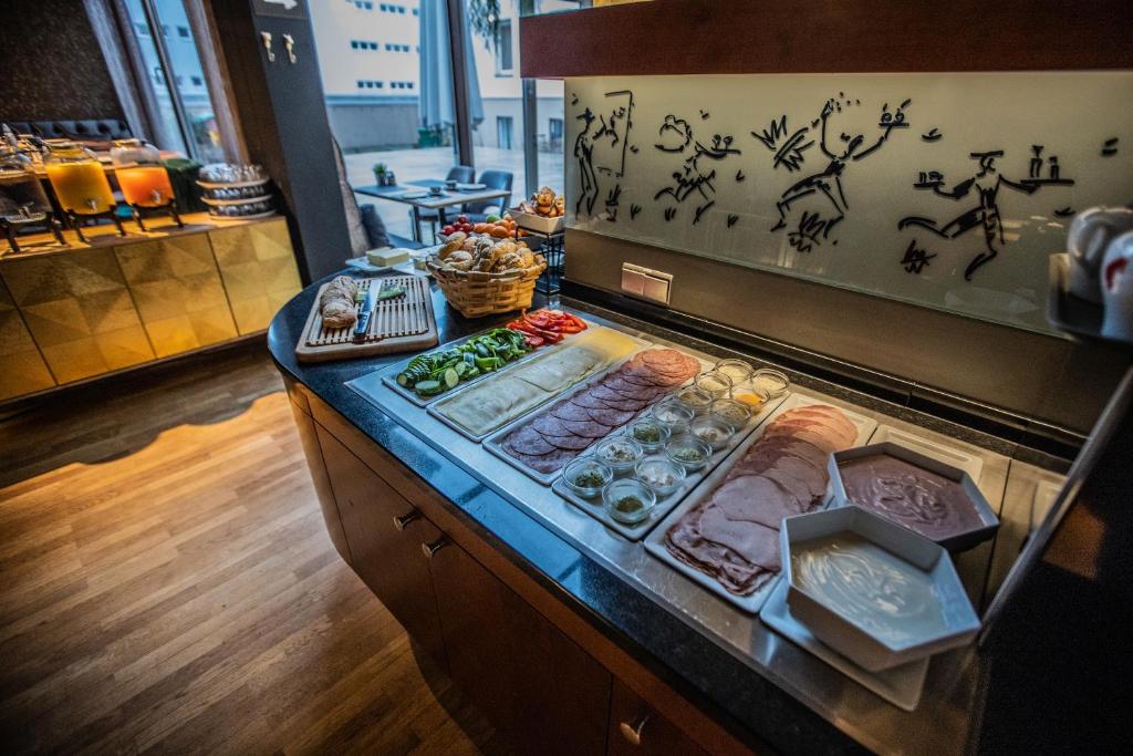 Pusdienu galda klāšana ar dažādiem gaļas produktiem, dārzeņiem un maizi, kas papildināta ar dekoratīvu sienu gleznojumu. Ideāli piemērots brokastu vai bufetes stila ēdienreizēm.