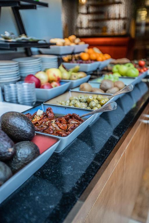 Bagātīgs augļu un dārzeņu bufete ar dažādām uzkodām un veselīgiem produktiem, ieskaitot avokado, žāvētus tomātus un dažādas augļu šķirnes.