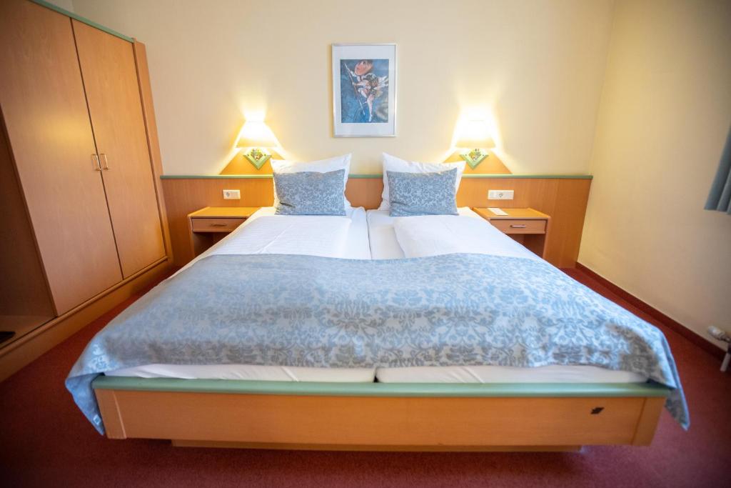 Mūsdienīga viesnīcas numura interjers ar divguļamo gultu, dekoratīvām spilveniem un gaismas elementiem. Telpa ir ērti iekārtota ar koka mēbelēm un mākslas darbu uz sienas.