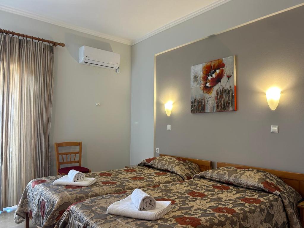 Gaiša viesnīcas istaba ar divām gultām, dekorētām ar ziedu rakstiem. Uz sienas ir mākslas darbs ar ziediem, un telpā ir gaisa kondicionieris un dabiska apgaismojuma avots.