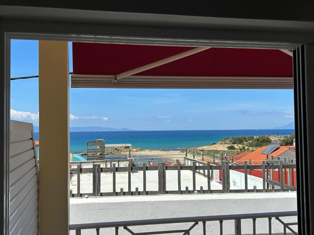 Skats no loga uz jūru ar smilšu pludmali un kalniem tālumā, kā arī jumtiem un terasēm tuvumā. Ideāla vieta atpūtai.