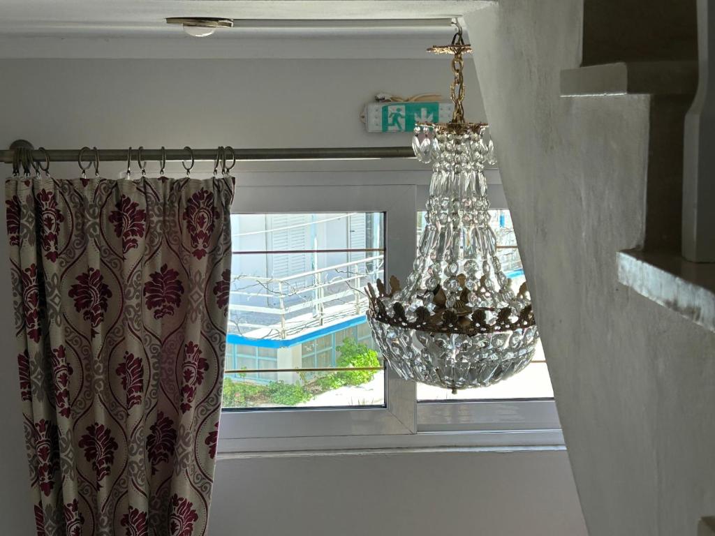 Lustras un aizkaru skats caur logu, kur redzams dārzs un peldbaseins. Elegantā lustrā ir daudz kristālu, kas piešķir telpai greznu izskatu.