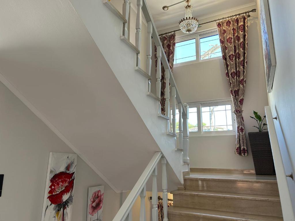 Mūsdienīga kāpņu telpa ar elegantu kristāla lustru, greznām aizkariem un mākslas darbiem uz sienām. Gaismas plūdums rada siltu un pievilcīgu atmosfēru.