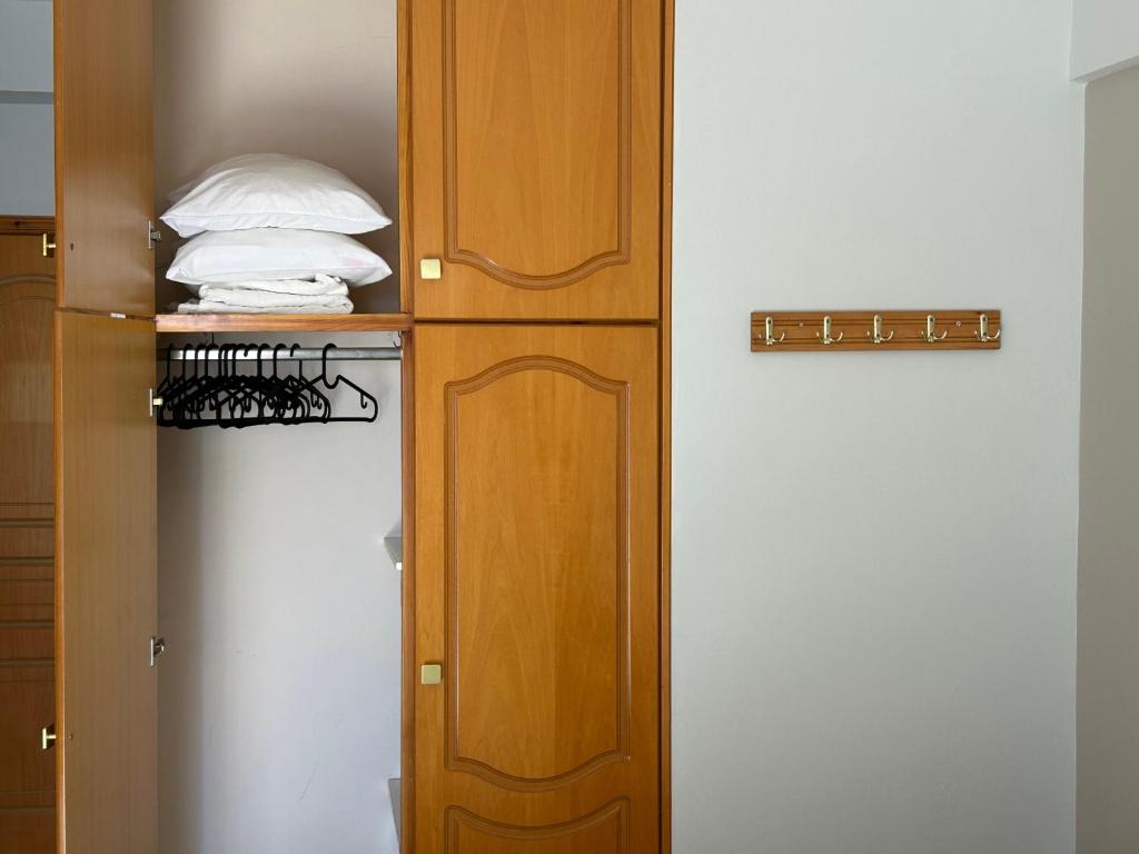 Koka skapīša iekšpuse ar salocītām spilveniem un drēbju pakarami. Blakus redzams āķu panelis, kas paredzēts apģērba vai aksesuāru piekāršanai.