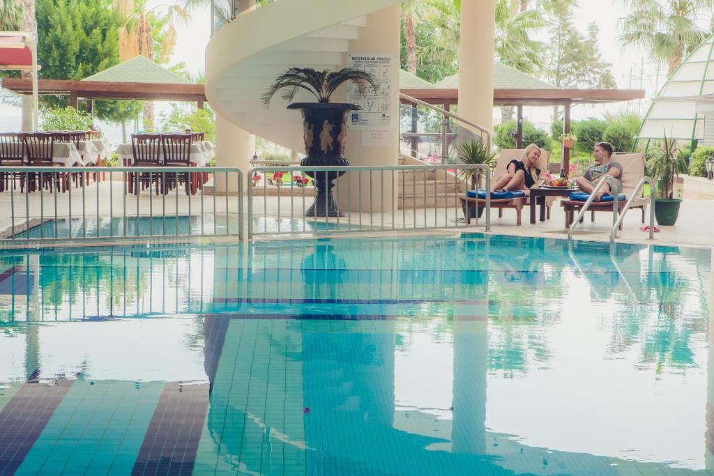 Pāris relaksējas pie baseina L'ancora Beach Hotel, baudot dzērienus un uzkodas.