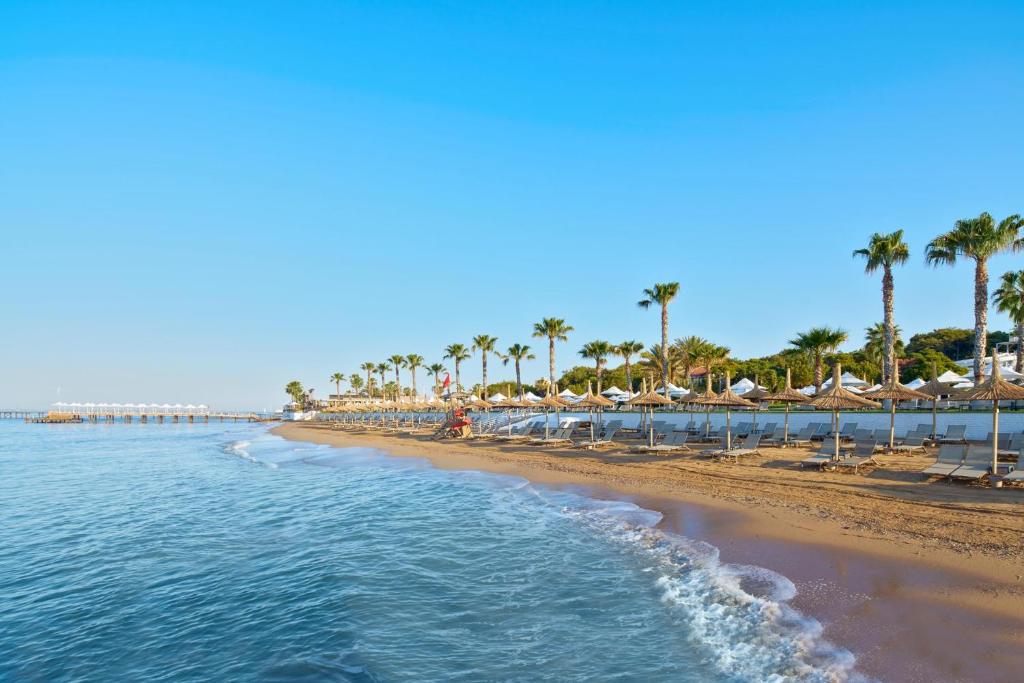 Pludmale pie Voyage Sorgun ar palmām un saulessargiem.