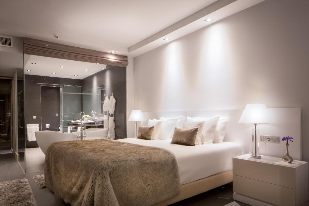 Mūsdienīgs guļamistabas interjers ar ērtu gultu, mēbelēm un stikla dušas kabīni. Telpa ir gaiša un eleganta ar siltām krāsām un modernām apgaismojuma iespējām.