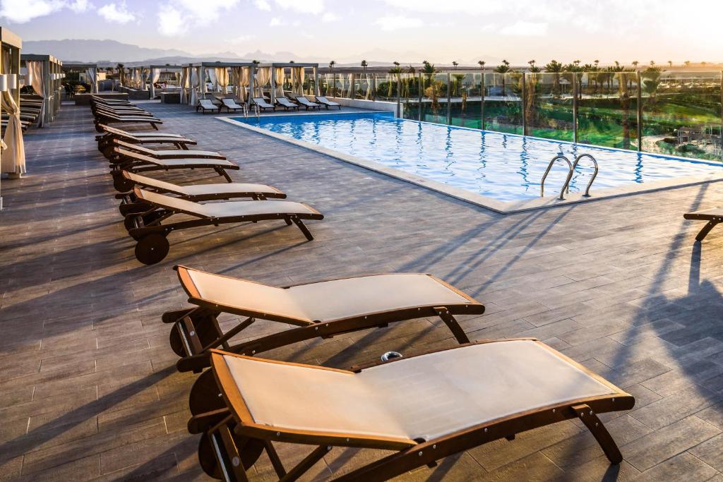 Jaz Aquaviva jumta baseins ar sauļošanās krēsliem saulrietā.
