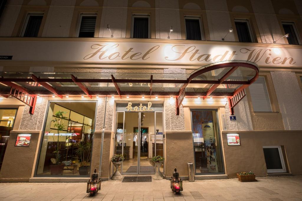 Viesnīcas "Hotel Stadt Wien" ieeja ar apgaismojumu un augstiem logiem, kas rada viesmīlīgu atmosfēru. Piebūvēti ziedi un dekoratīvi elementi piešķir šarmu.