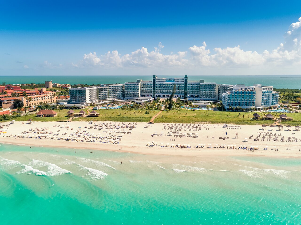 Piekrasna pludmale ar viesnīcu, kas atrodas tieši pie ūdens, un pludmales krēslu rinda, kas gaida apmeklētājus. Skaists skats uz zilo jūru un debesīm. panoramic view with beach and pools
