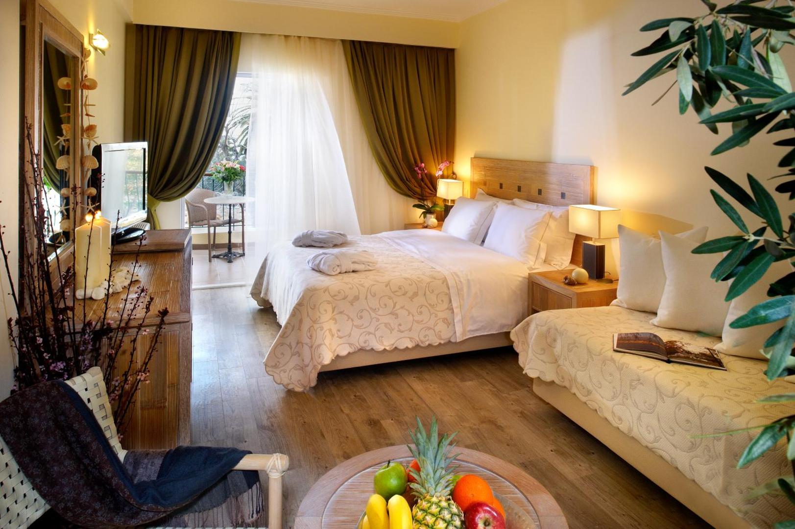 Portes Beach Hotel mājīgs numurs ar koka apdari, dīvānu un augļu plati priekšplānā Halkidiki — silts apgaismojums un terase