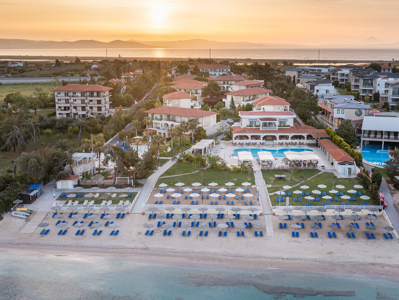 Portes Beach Hotel panorāmas skats no augšas uz kūrorta teritoriju, baseinu un pludmali Halkidiki piekrastē saulrieta laikā