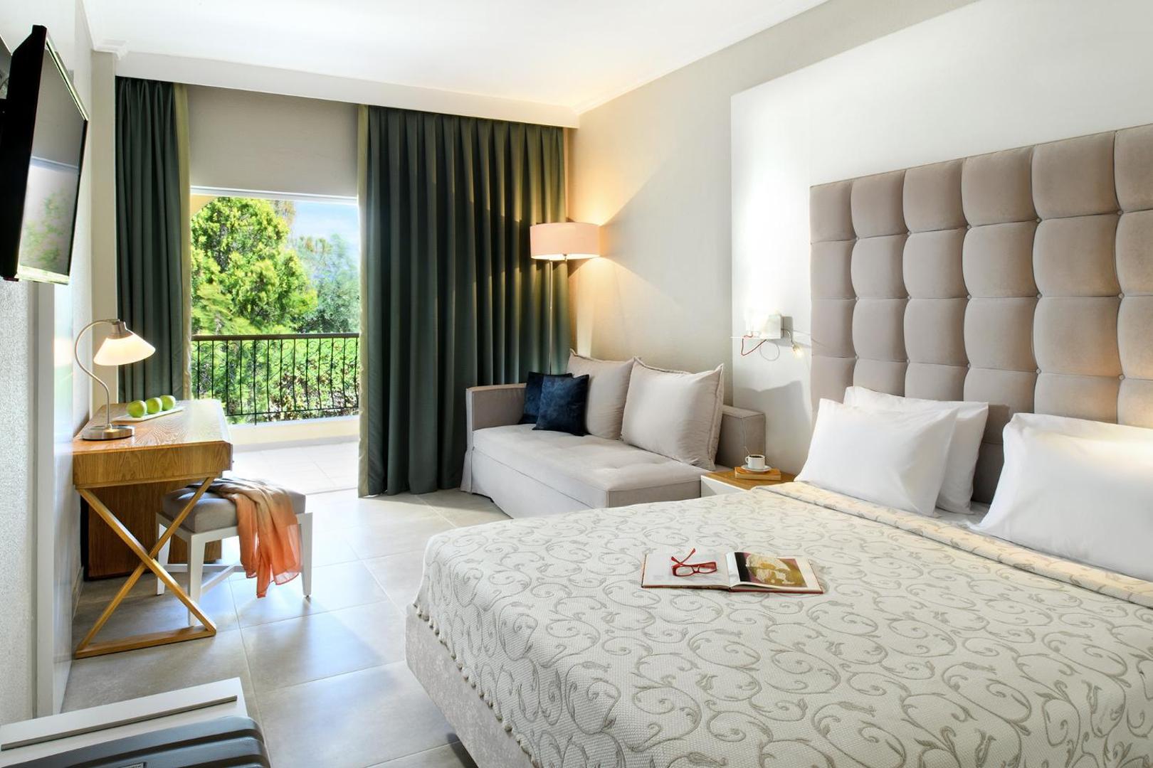 Portes Beach Hotel gaišs numurs ar divguļamo gultu, dīvānu un balkonu Halkidiki reģionā — skats uz zaļojošu dārzu caur lielu logu