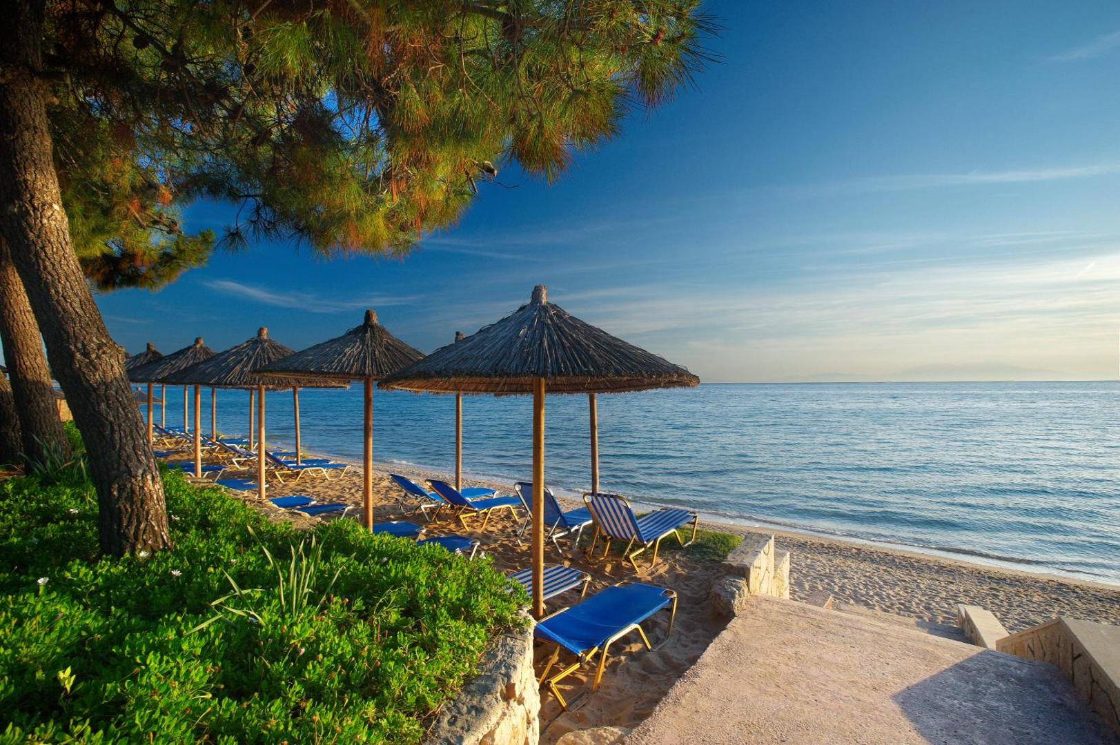 Portes Beach Hotel pludmales zona ar saulessargiem un zviļņiem priežu meža ēnā pie Egejas jūras