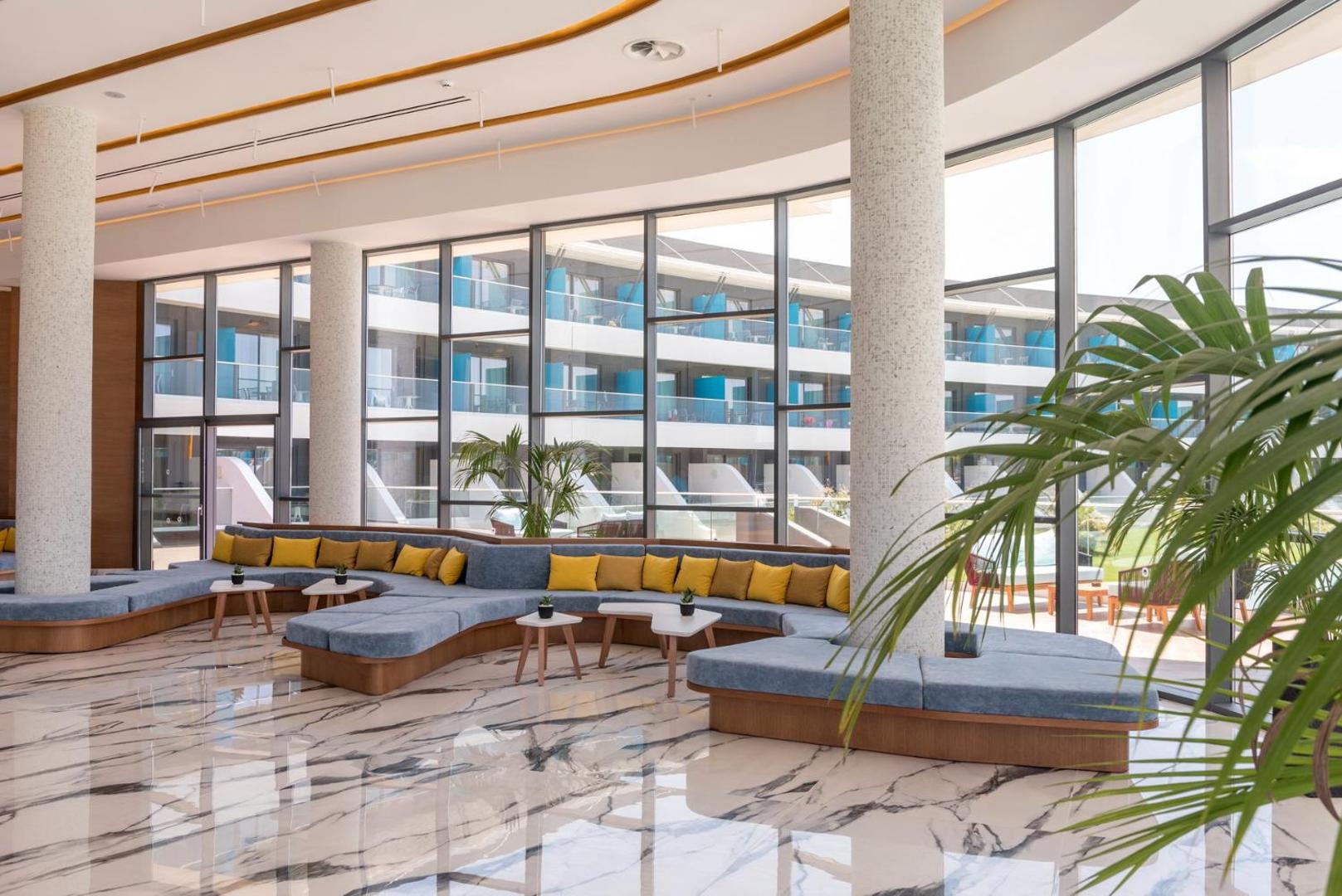Lyttos Mare viesnīcas plašā lobby atpūtas zona ar marmora grīdu, lieliem logiem un moderniem dīvāniem Hersonisā, Krētā