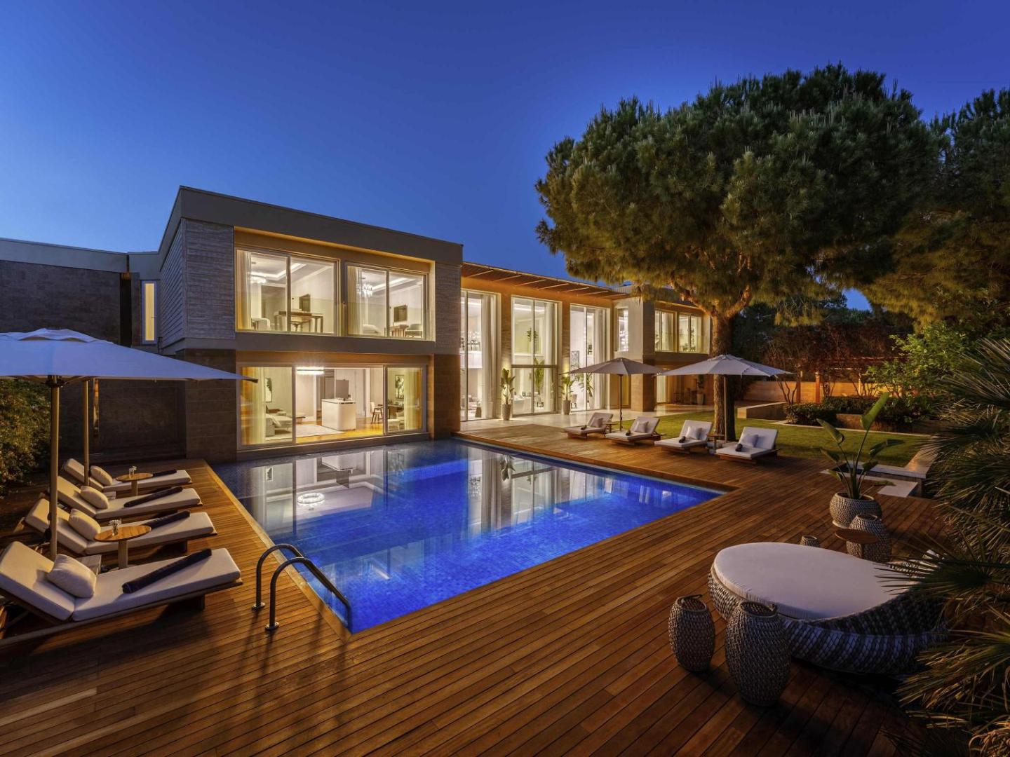 Rixos Premium Belek villas vakara apgaismojums ar izgaismotu baseinu, terasi un lieliem panorāmas logiem Belekas kūrortā