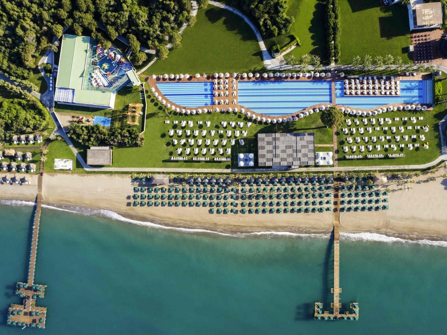 Rixos Premium Belek viesnīcas skats no putna lidojuma uz plašo piekrasti, āra baseiniem, pludmali un divām koka piestātnēm Antaljas reģionā
