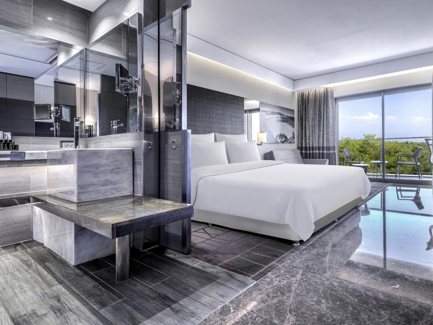 Rixos Premium Belek moderns viesnīcas numurs ar marmora apdari vannas istabas zonā, plašu gultu un balkonu ar skatu uz priežu mežu