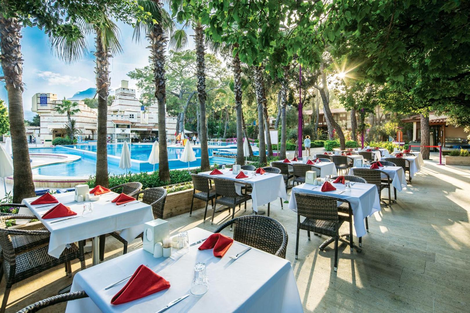 Ulusoy Kemer Holiday Club āra restorāna terase ar galdiņiem zem palmām pie baseina Kemeras kūrortā