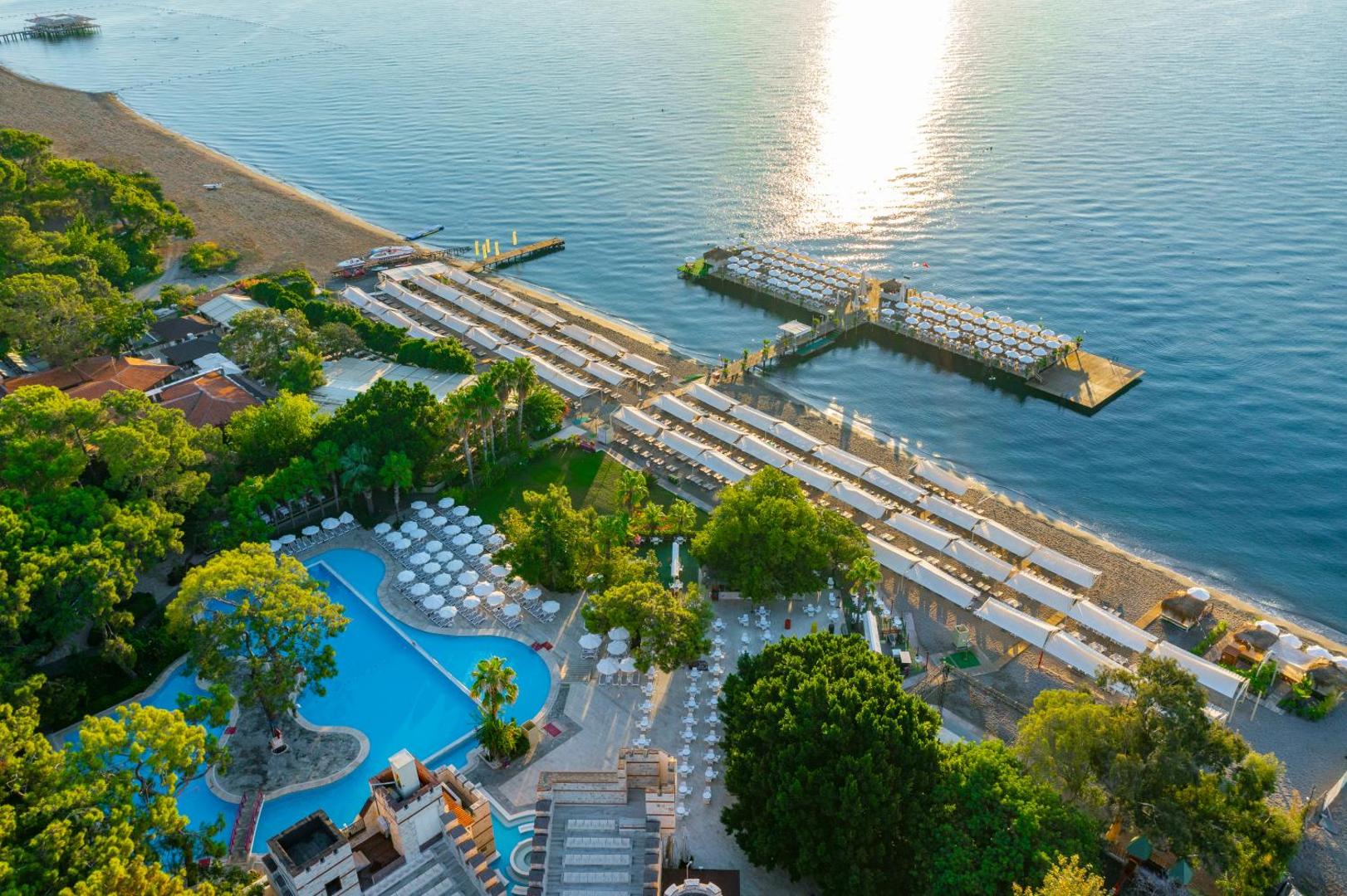 Aerofoto skats uz Ulusoy Kemer Holiday Club teritoriju ar baseiniem, privāto pludmali un piestātnēm saulrieta gaismā