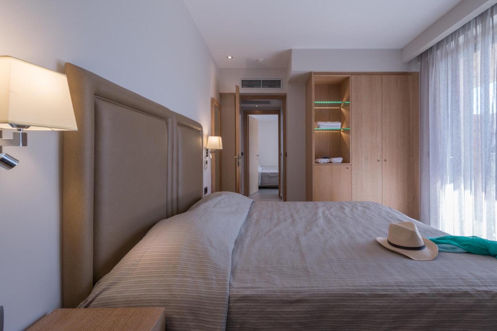 Moderns viesnīcas numurs ar lielu gultu, koka skapi un gaišiem aizkariem.