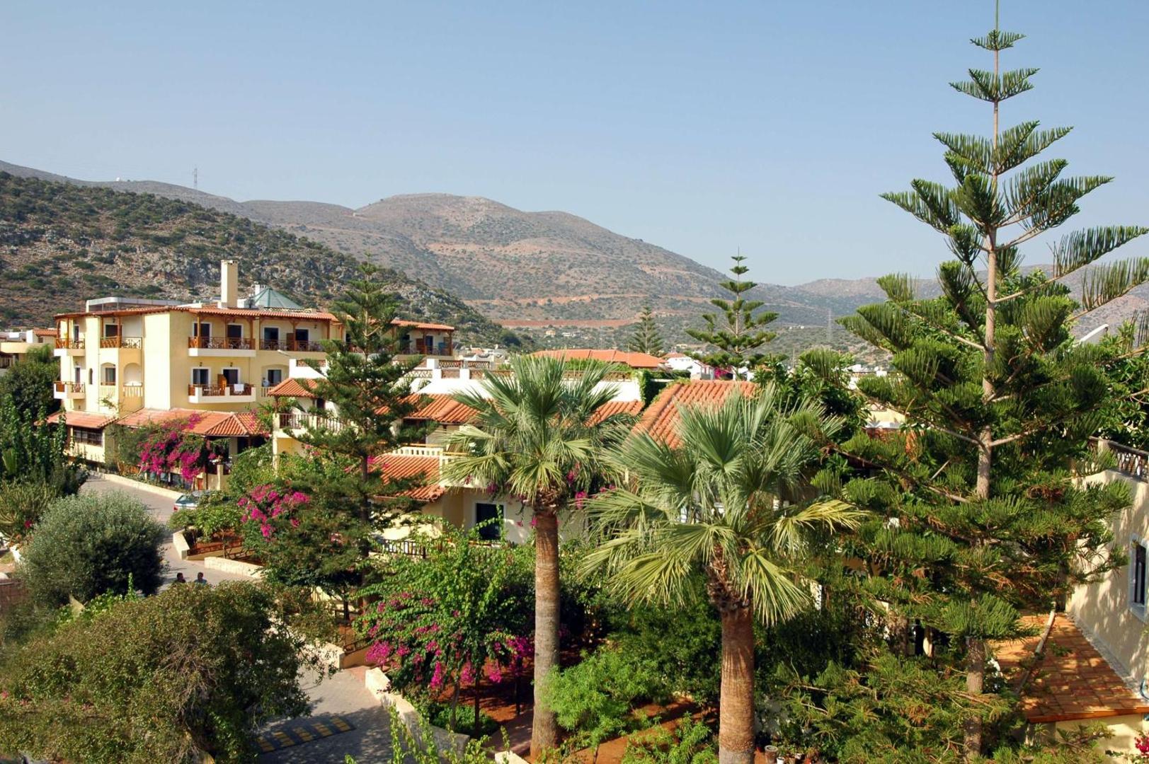 Skats no augšas uz viesnīcas dārzu, palmām un kalniem fonā.