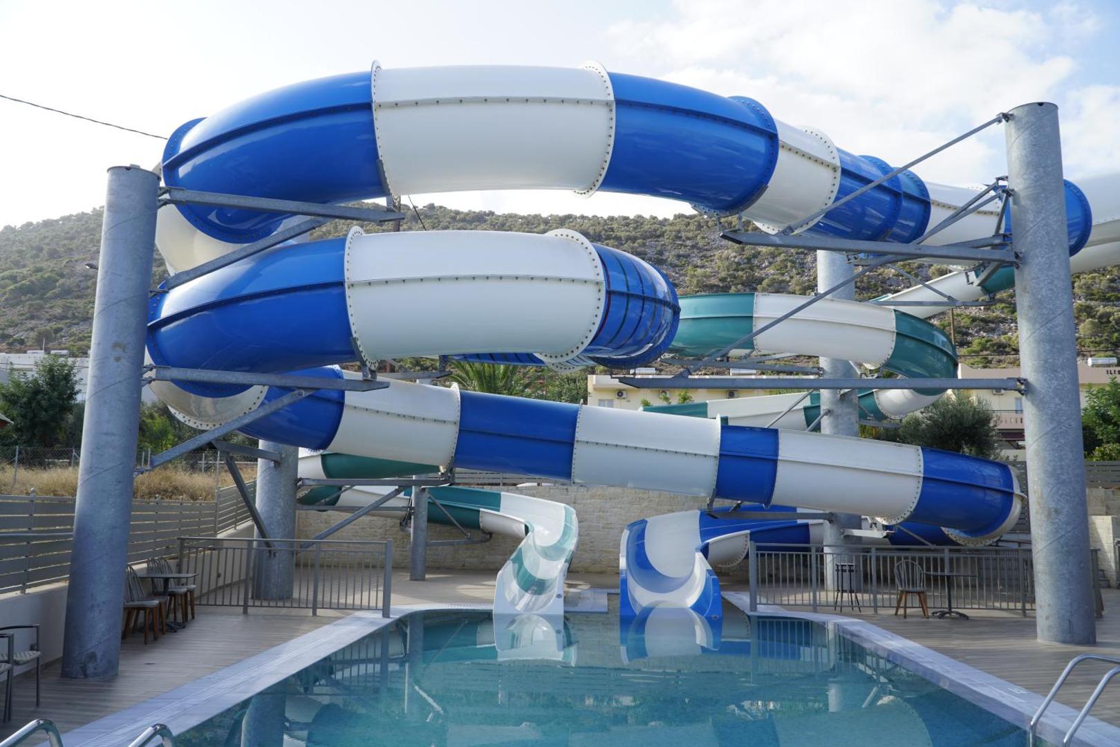 Liels zili balts ūdens slidkalniņš pie āra baseina saulainā dienā.